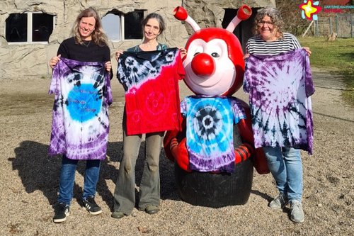 Die Mitarbeiterinnen des Grünen Klassenzimmers mit gebatikten T-Shirts. Sie stehen neben einer Rieti-Figur, die ebenfalls ein gebatiktes T-Shirt trägt.