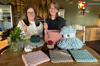 Julia Wittreck und Silke Lühnen-Schilling stehen im Emsbräustübchen hinter einem Stehtisch, auf dem gehäkelte Dinge liegen.