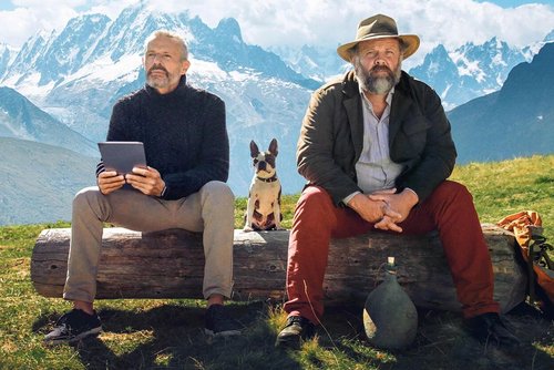 Filmplakat: Zwei Männer sitzen vor malerischer Bergkulisse auf einem Baumstamm und schauen in die Ferne.