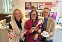 Die Touristik-Mitarbeiterinnen mit Utensilien der Lukullischen Führungen: Weingläser und -flaschen, Kaffeetassen, Kochlöffel etc.
