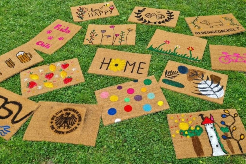 Bunt bemalte Fußmatten liegen auf einer Wiese.