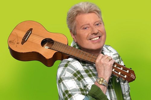 Kinderliedermacher Volker Rosin mit Gitarre auf der Schulter vor einer grünen Wand.