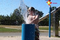 Ein Junge auf dem Wasserspielplatz hinter einer Wasserfontäne.