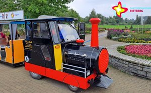 Eine schwarze Lok mit rotem Schornstein rollt durch einen Park mit Blumenbeeten.