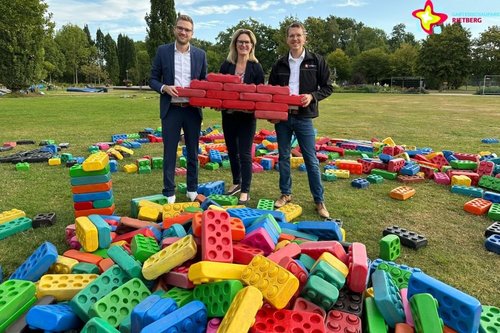 Sparkassen-Vertreter und Park-Geschäftsführer stehen zwischen den Bausteinen und halten rote Bausteine in der Hand.