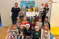 Heike Krause und Johannes Wiethoff mit den Kindern in der Turnhalle, einige sitzen oder knien auf einer großen Turnmatte, andere sitzen auf einem großen Kasten.