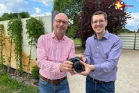 Frank Ehlebracht und Johannes Wiethoff stehen vor den Sichtschutzwänden und halten eine Fotokamera in den Händen.