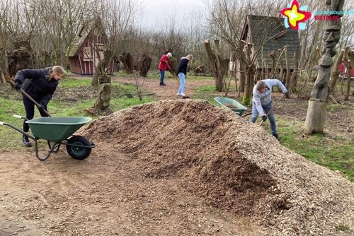 Zu sehen sind Helfer, die Rindenmulch in Schubkarren schaufeln und verteilen. Im Hintergrund sind die Hexenhäuschen zu sehen.