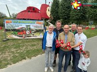 Die genannten Personen stehen im Park vor einem großflächigen Plan, der das neue Spielgerät zeigt. Im Hintergrund steht das alte Rieti-Spielgerät.