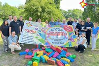 Teilnehmer der Entdeckerzone, Organisatoren und Veranstalter mit einem großen Radio-Gütersloh-Sommerfest-Banner. Im Vordergrund sind die Großbausteine von der Picknickwiese im Gartenschaupark zu sehen.