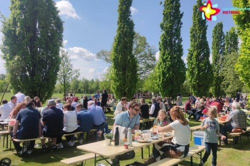 Familien sitzen an Bierzeltgarnituren und lassen es sich beim Picknick schmecken.
