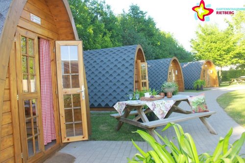 Zu sehen sind vier Camping Pods. Vor einem steht ein gedeckter Tisch.