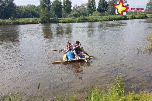 Zu sehen ist ein Kanu mit zwei Menschen, die sich mit Paddeln vom Ufer abstoßen.