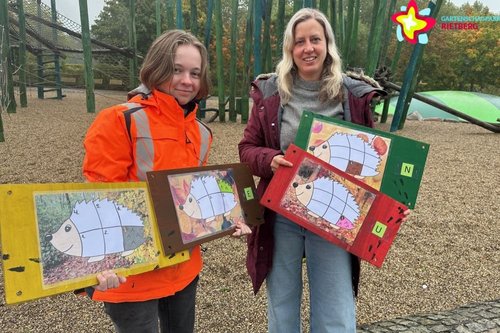 Andrea Sassenberg und Leah Schmelz mit den Rätseltafeln, auf denen jeweils ein großer Igel zu sehen ist, vor dem Spielplatz Schilfwald.