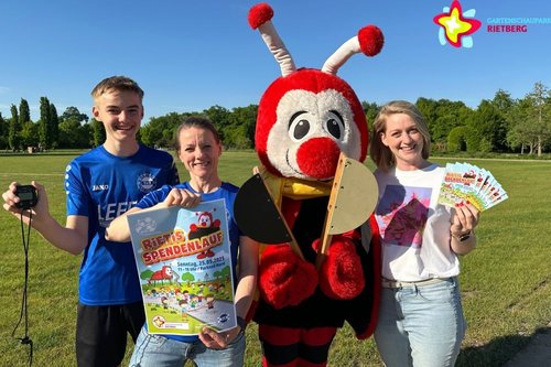 Maskottchen Rieti mit Emil und Jessica Nöcker vom TuS Viktoria Rietberg und Verena Reinkemeier vom Gartenschaupark Team. Rieti hält eine Startklappe in Händen, Emil Nöcker eine Stoppuhr, Jessica Nöcker ein Plakat und Verena Reinkemeier Flyer zum Spendenlauf.