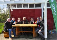 GNU-Gartenteam und Parkleitung sitzen vor dem GNU-Pavillon und stoßen mit eine Gläschen Sekt an.