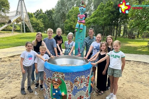 Karin Wolf, Johannes Wiethoff und die jungen Künstler stehen um den neuen Brunnen herum. alle legen eine Hand an das neue Kunstwerk, um zu zeigen: Diesen Brunnen haben wir gemeinsam entworfen und gebaut.