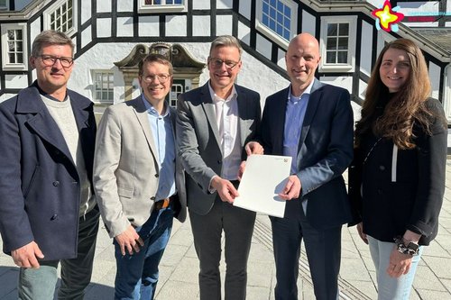 Abteilungsleiter Kronsbein von der Bezirksregierung Detmold, Bürgermeister Andreas Sunder und Gartenschaupark-Mitarbeiter mit Förderbescheid vor dem Rathaus.