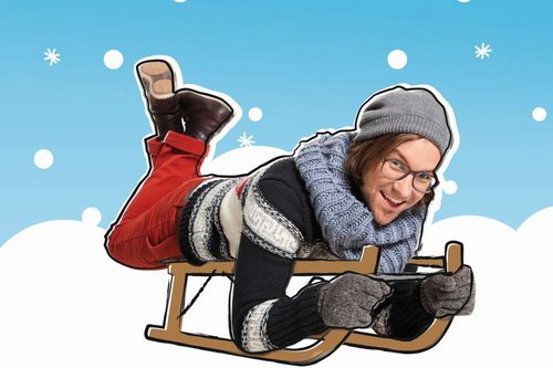 Kinderliedermacher herrH, winterlich gekleidet, liegt auf dem Bauch auf einem Schlitten.