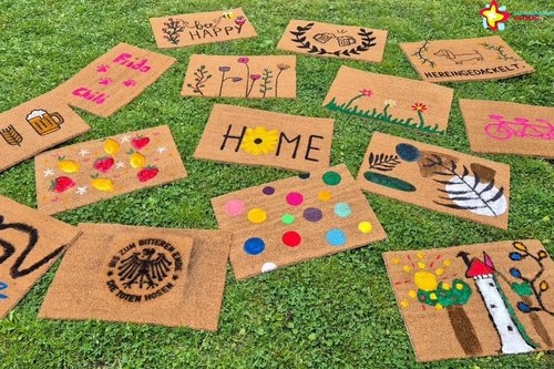 Bunt gestaltete Fußmatten liegen auf einer Wiese.