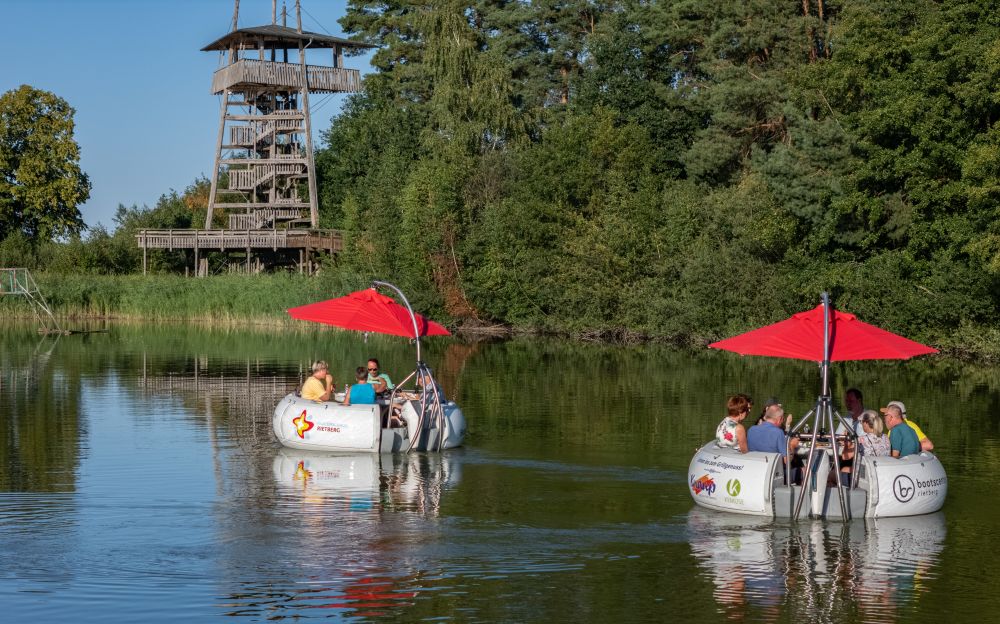 Auf dem Wasser fahren die BBQ-Boote.
Dahinter steht ein Aussichts-turm.