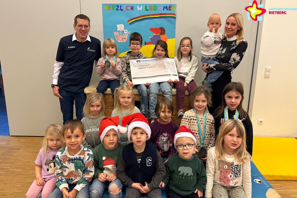 Heike Krause und Johannes Wiethoff mit den Kindern in der Turnhalle, einige sitzen oder knien auf einer großen Turnmatte, andere sitzen auf einem großen Kasten.