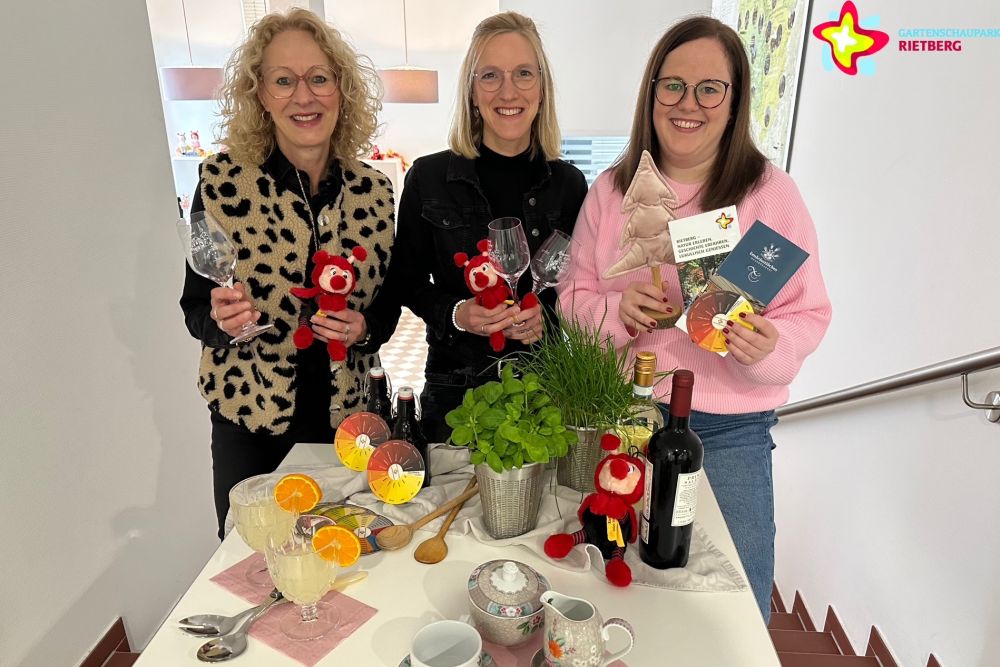 Die Mitarbeiterinnen der Touristikinformation stehen hinter einem gedeckten Tisch, in der Hand Weingläser, Mini-Rietis und Flyer.