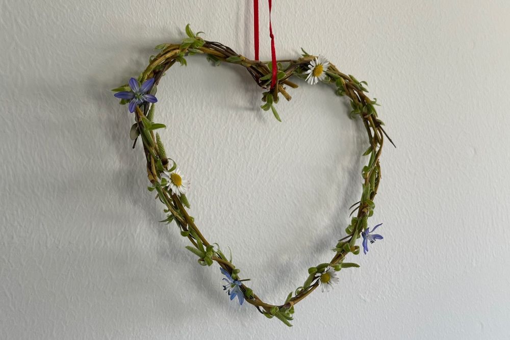 Herzchen aus Frühlingsgrün, das an einer Wand hängt.