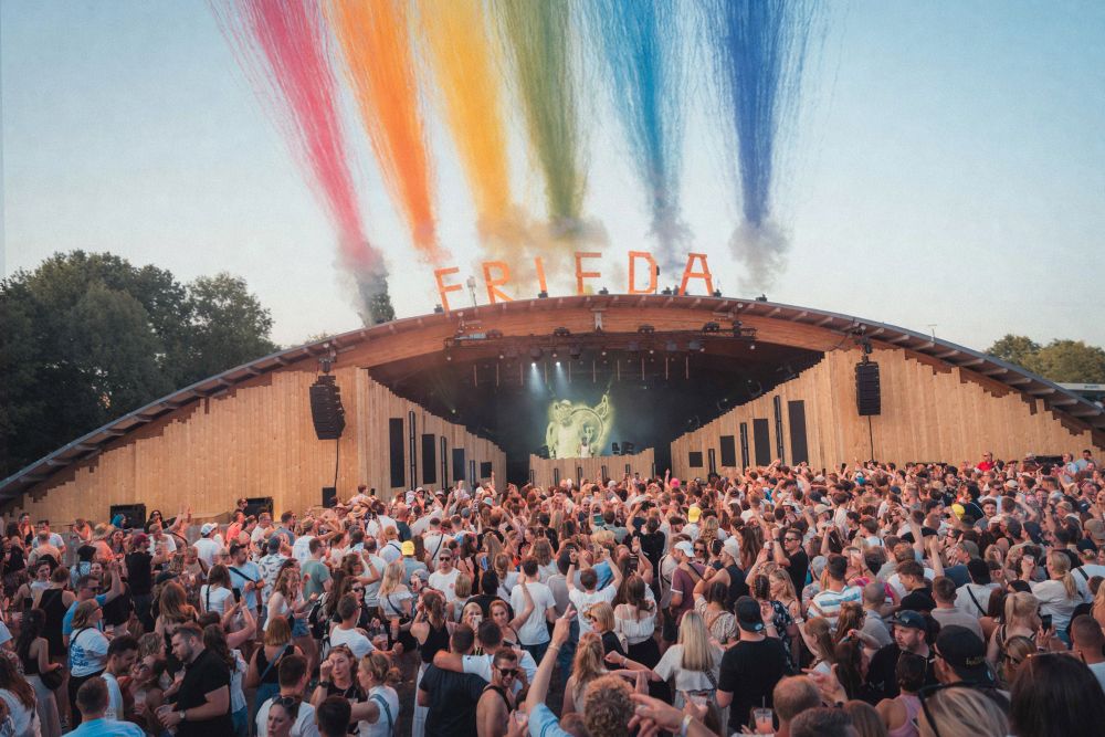 Blick auf die Hauptbühne bei Friedas Tanztee, die Volksbank-Arena. Im Vordergrund feiernde Menschen. Über den F-R-I-E-D-A-Buchstaben auf dem Dach der Arena bunte Fontänen.