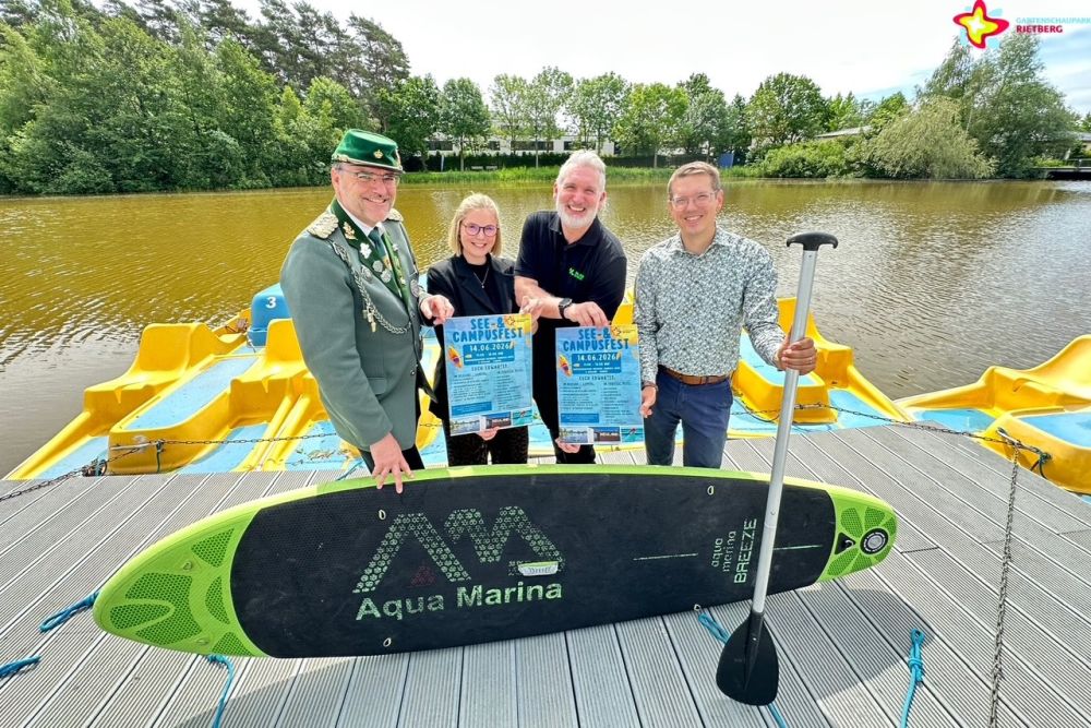 Veranstalter und Aktive des See- und Campufestes stehen auf dem Tretboot-Steg am Obersee, halten Plakate fürs See- und Campusfest in den Händen. Vorne ist ein Stand-Up-Paddleboard zu sehen.